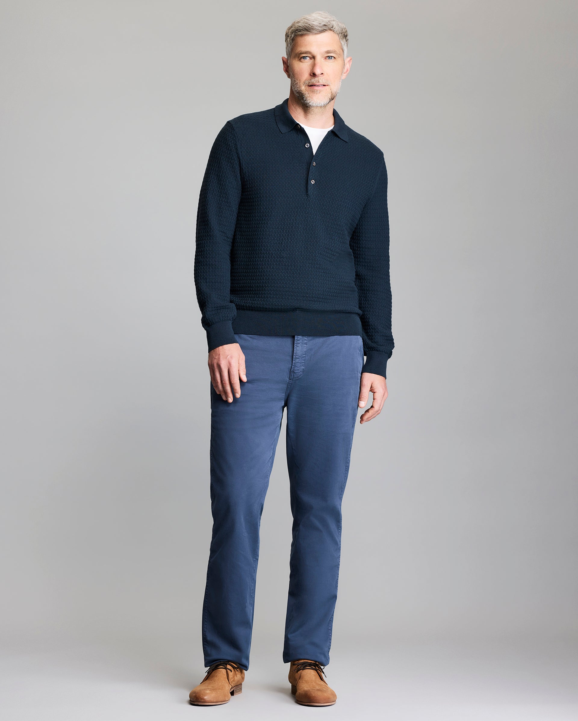 Man wearing a navy sweater and blue pants on a gray background