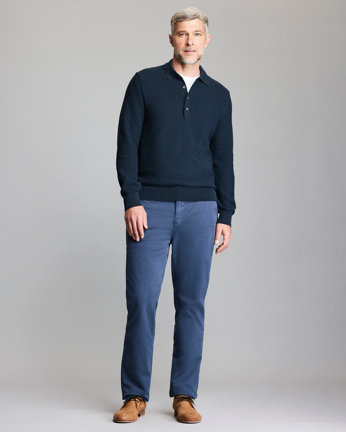 Man wearing a navy sweater and blue pants on a gray background