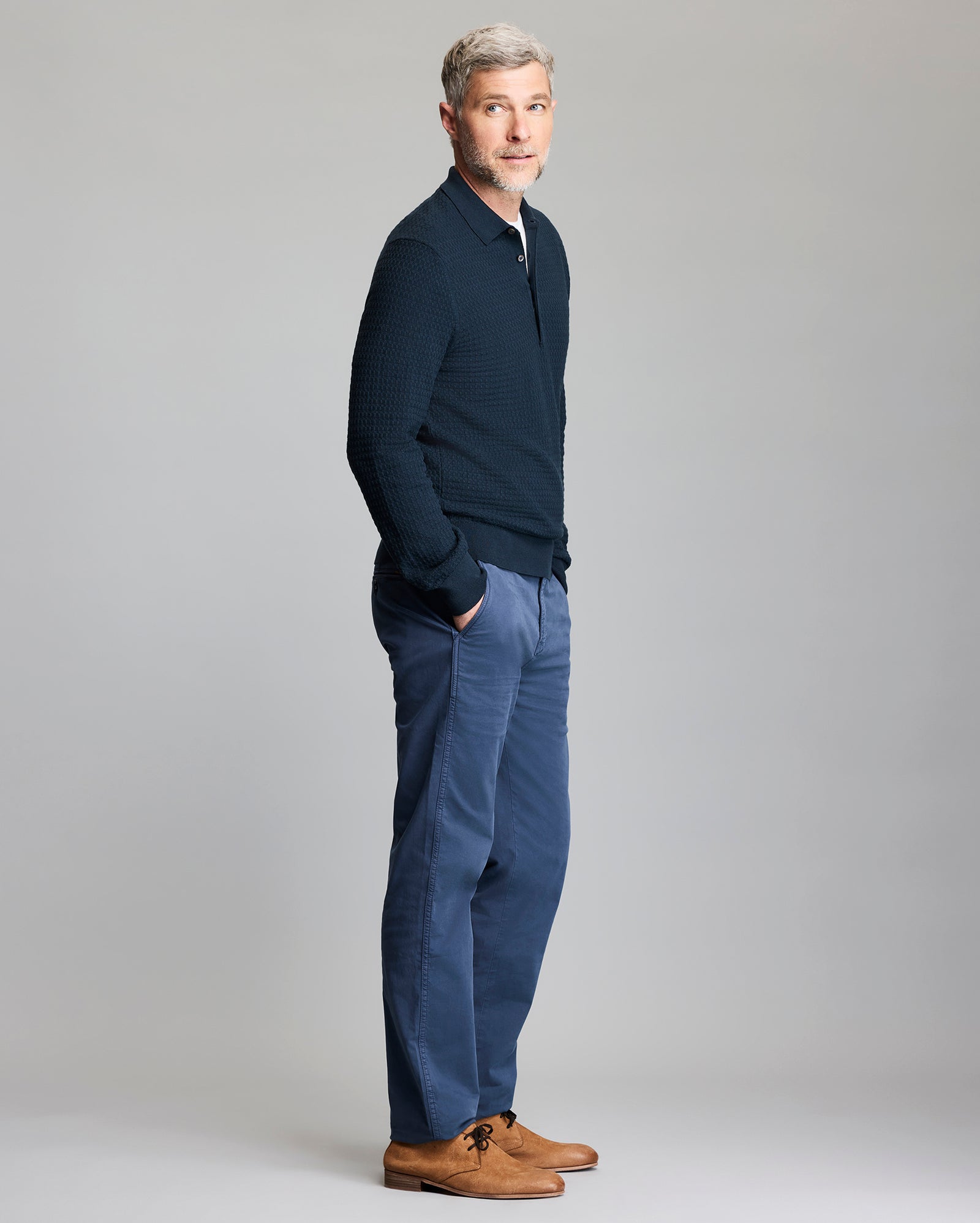 Man wearing a navy sweater and pants with brown shoes on a gray background