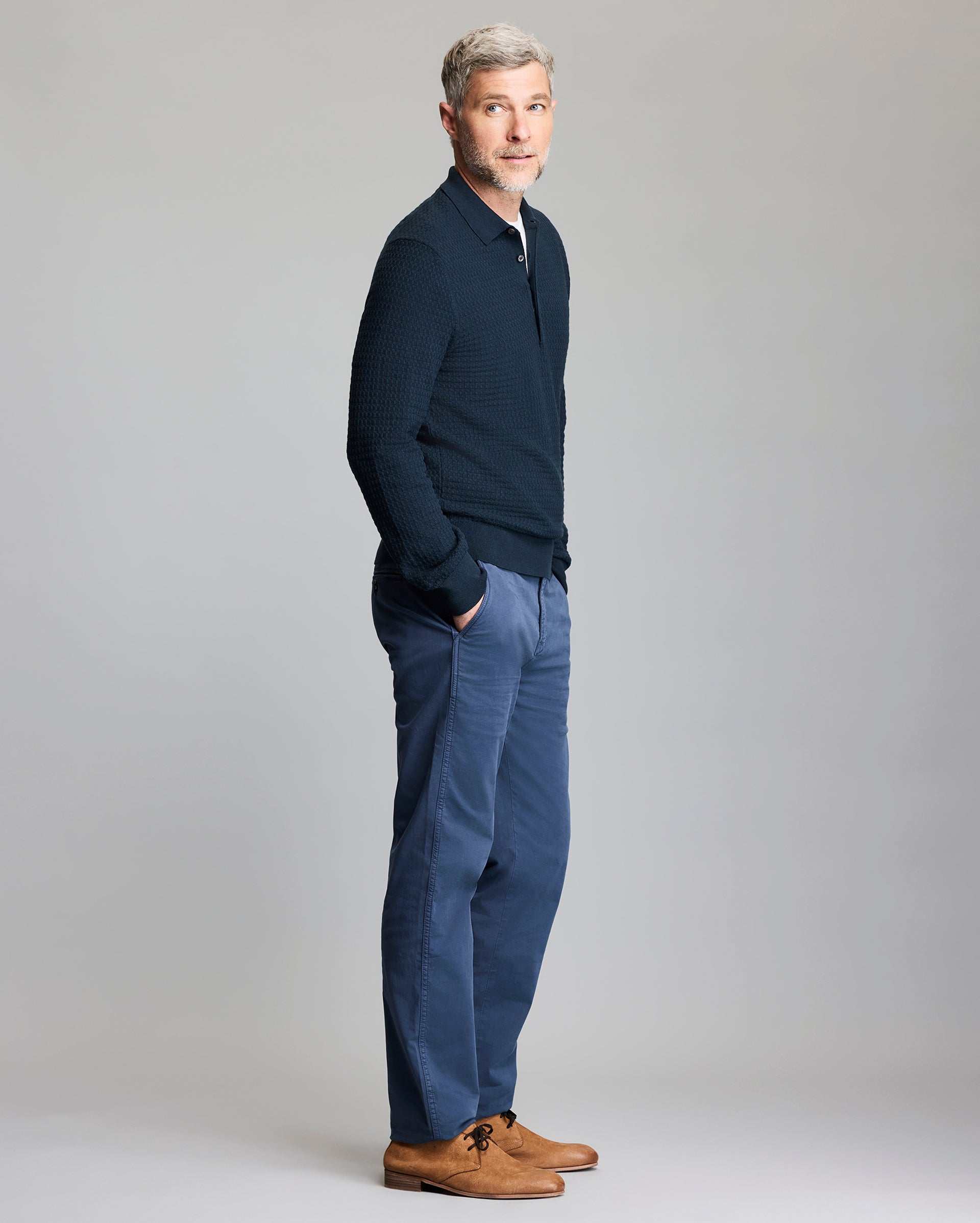 Man wearing a navy sweater and pants with brown shoes on a gray background