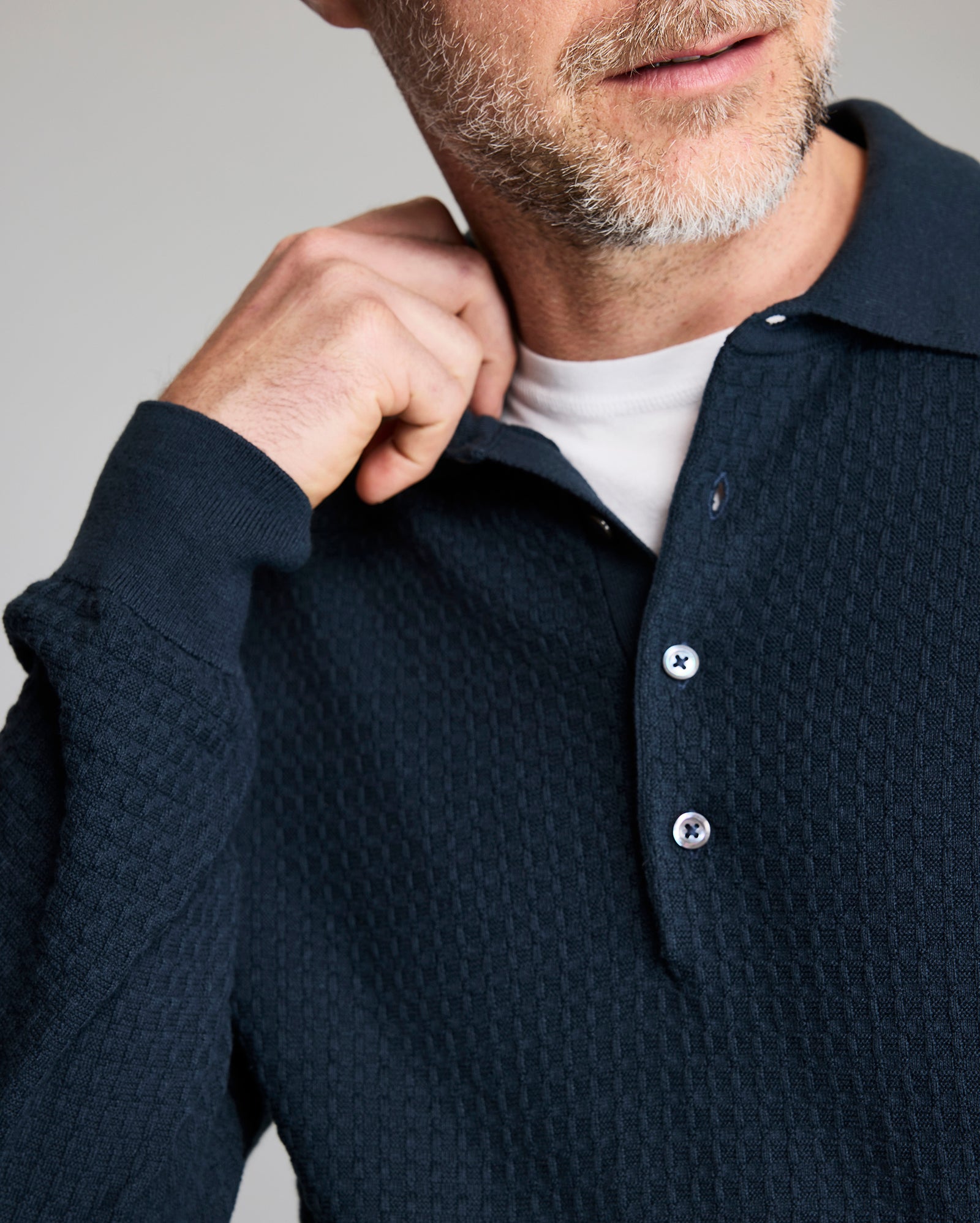 Man wearing a navy blue textured sweater with a white shirt underneath on a gray background