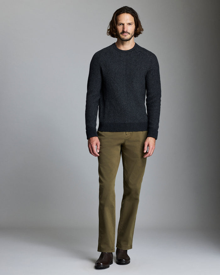 Man wearing a dark sweater and green pants against a gray background