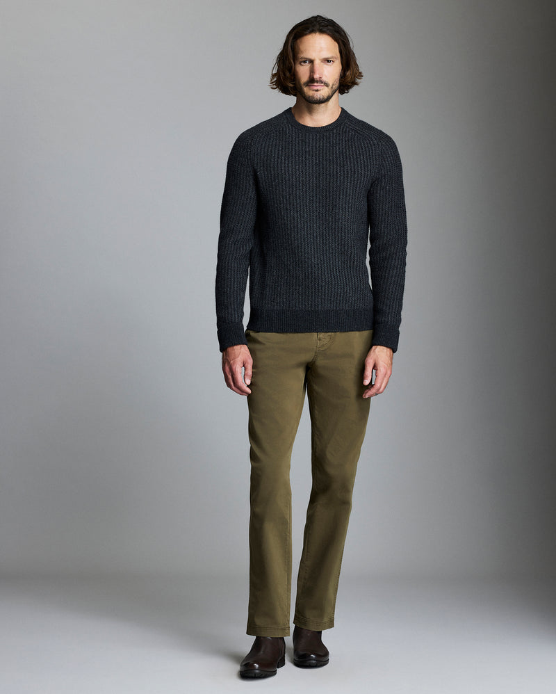 Man wearing a dark sweater and green pants against a gray background Alternate