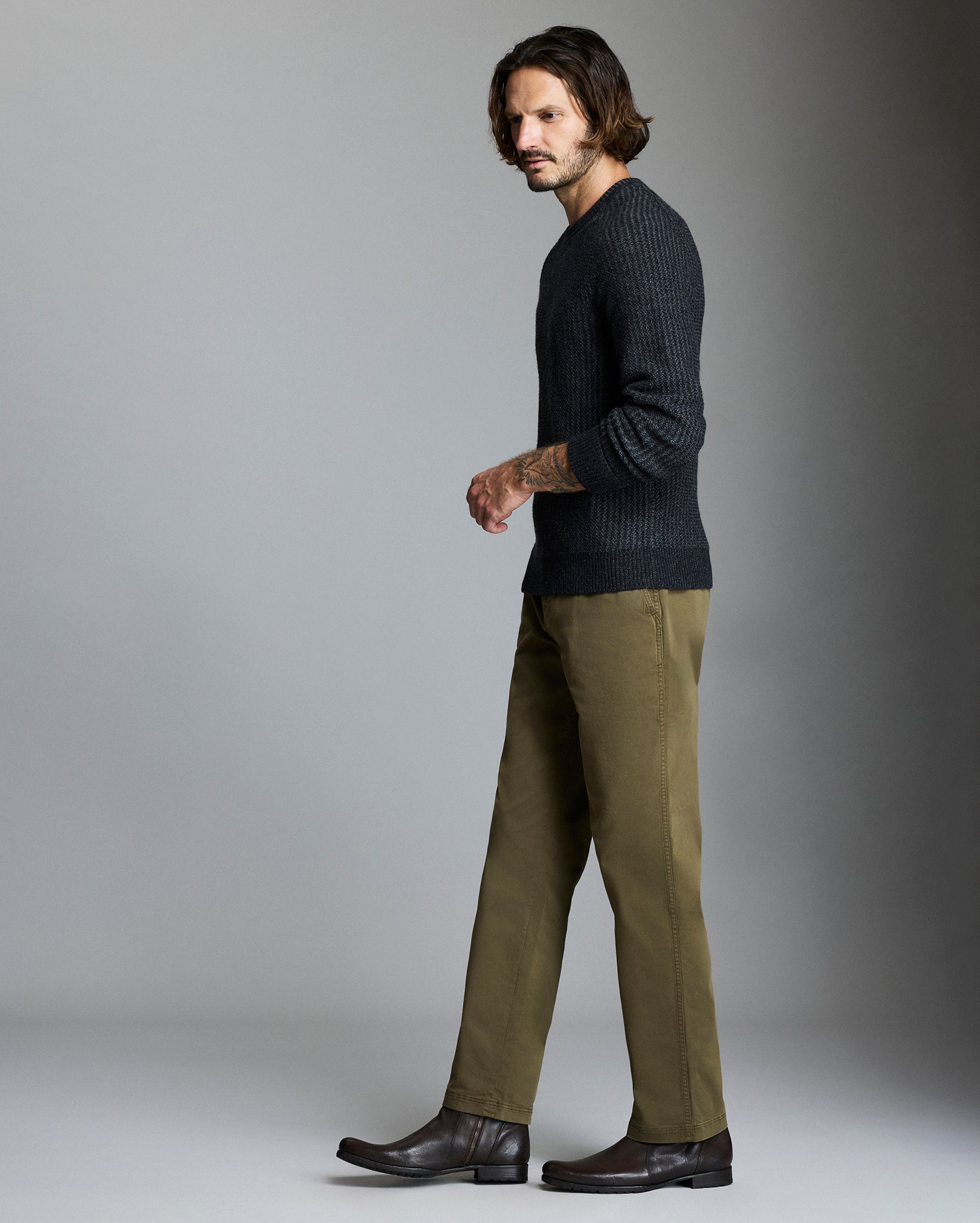 Man wearing a dark sweater and green pants against a gray background