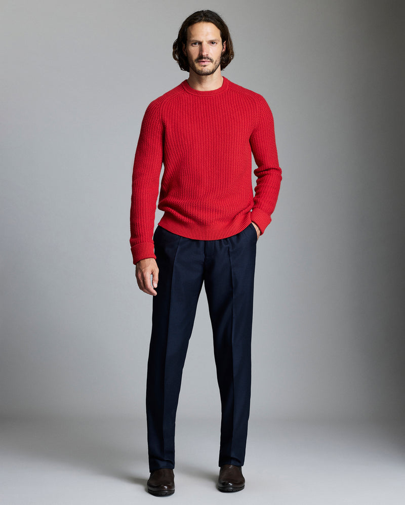 Man wearing a red sweater and navy pants against a gray background Alternate