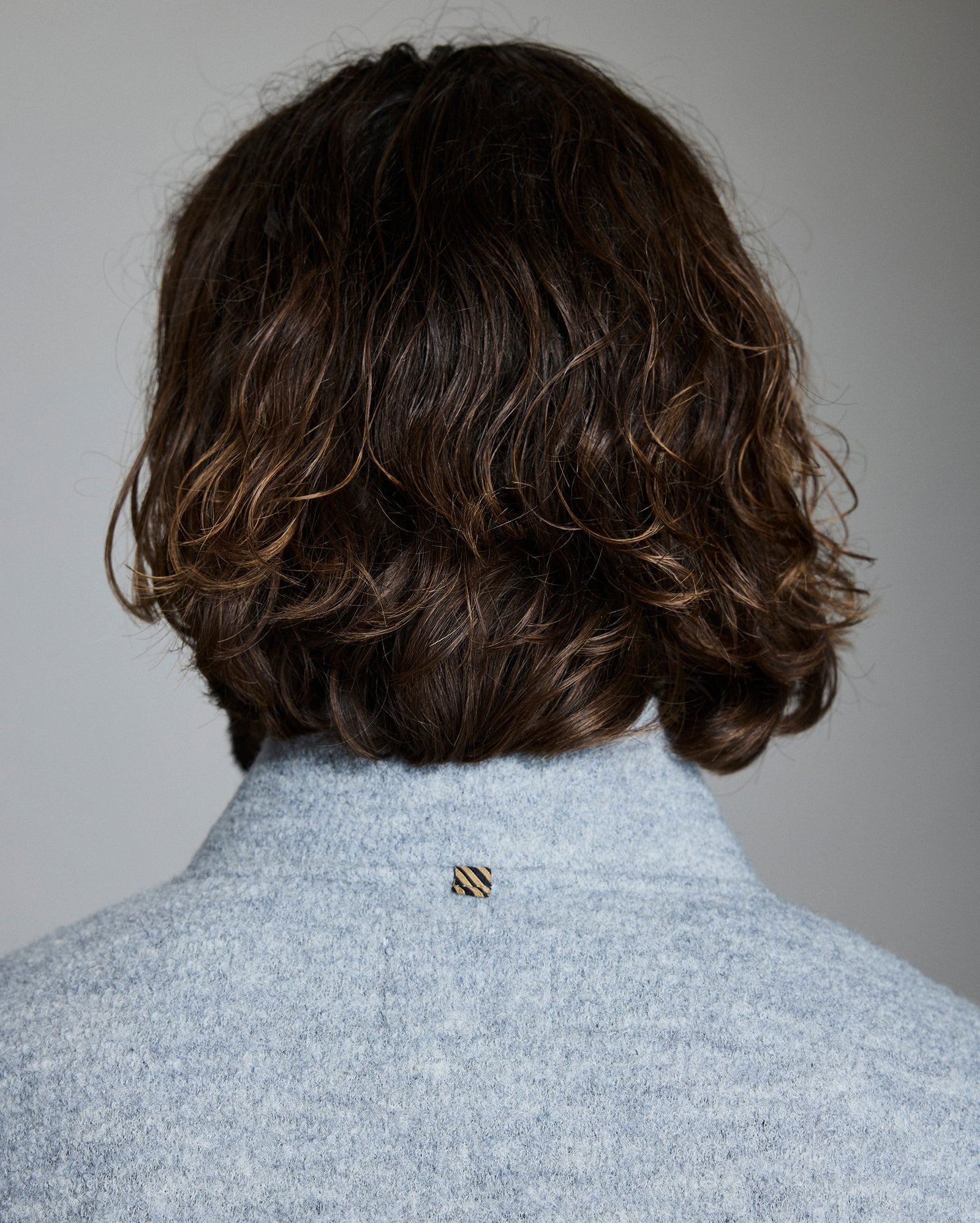 Back view of a person wearing a light gray coat with a brand logo on a plain background