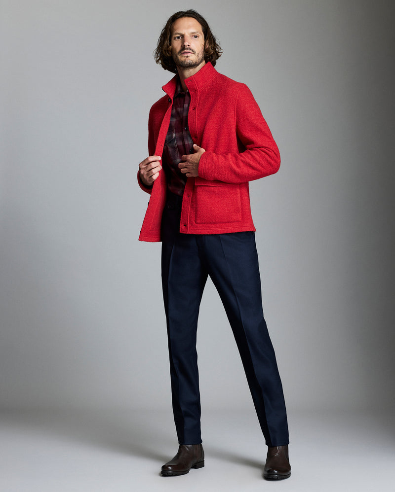 Man wearing a red jacket over a plaid shirt with navy pants against a gray background Alternate