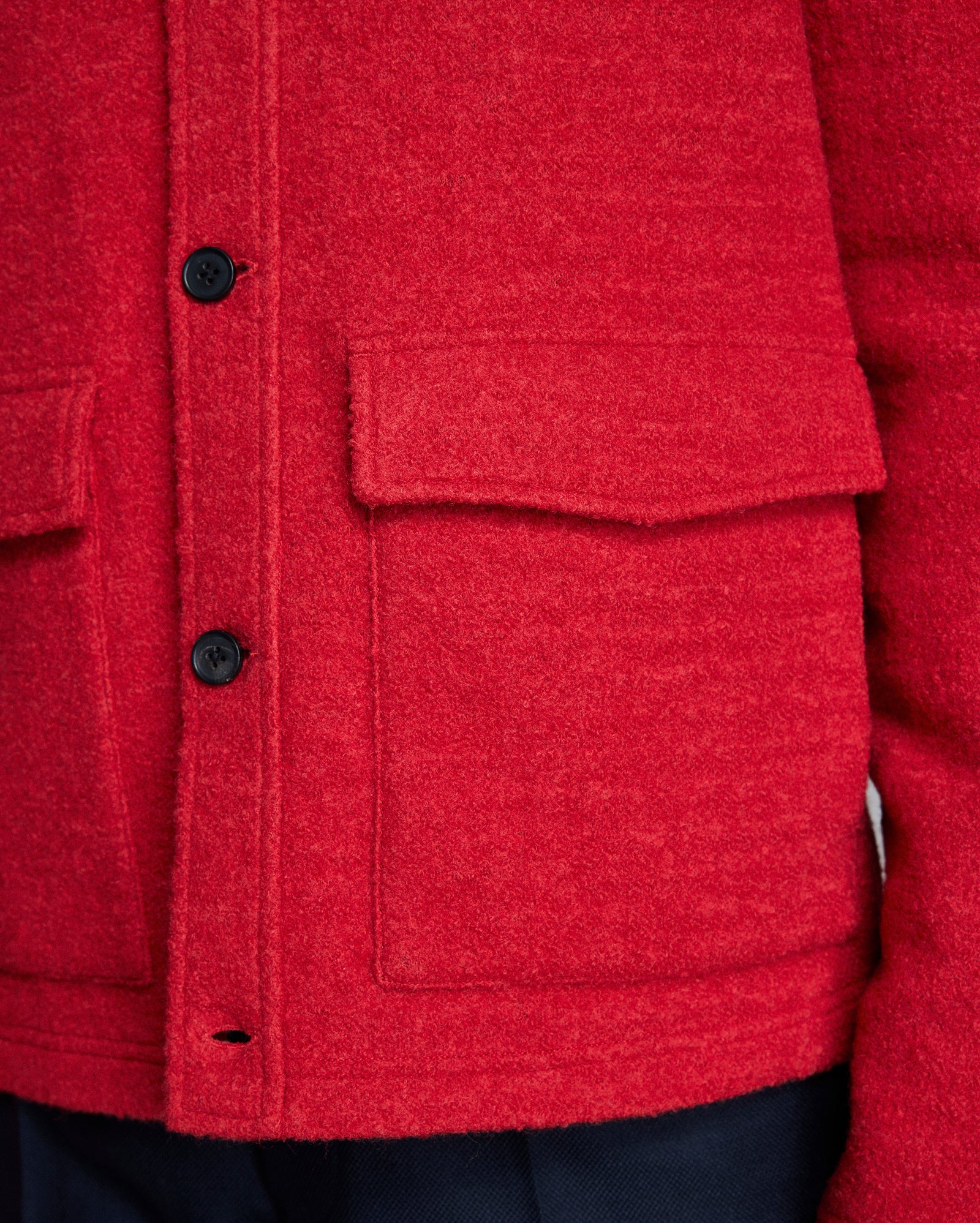 Close-up of a red textured jacket with buttons and pockets.