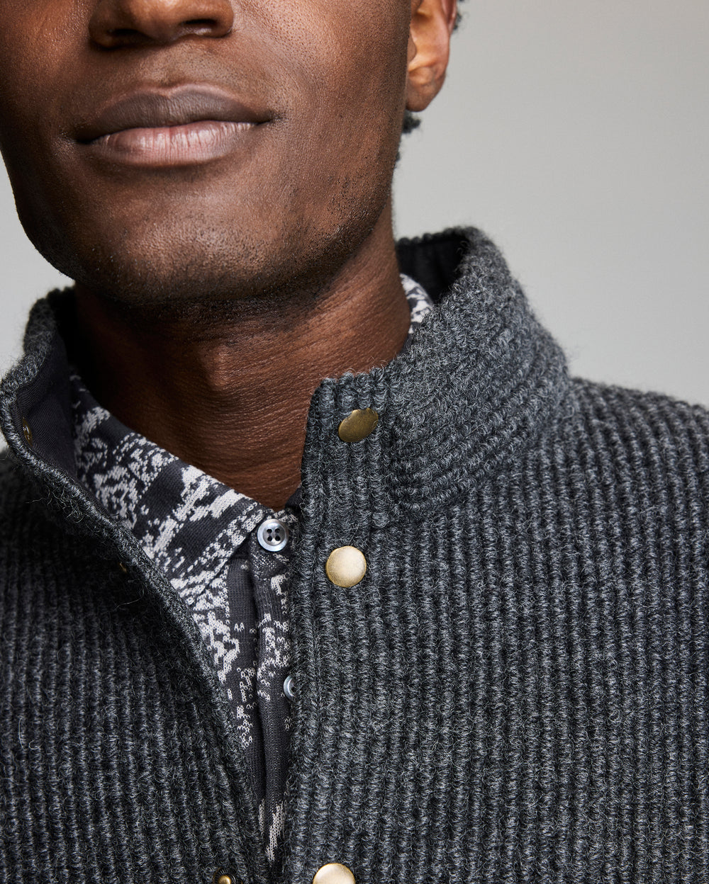 Close-up of a person wearing a textured gray jacket with a patterned shirt underneath.