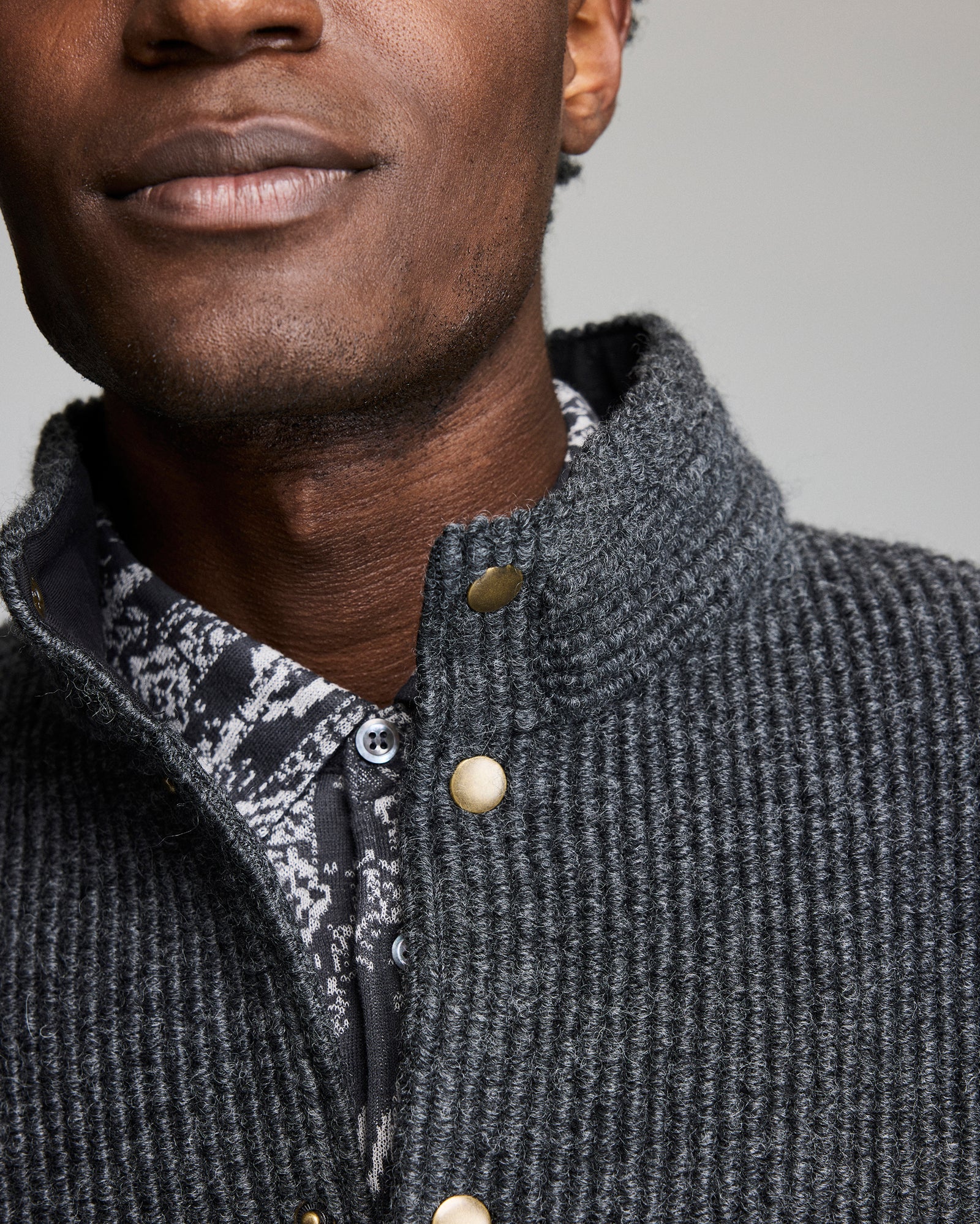 Close-up of a person wearing a textured gray jacket with a patterned shirt underneath.