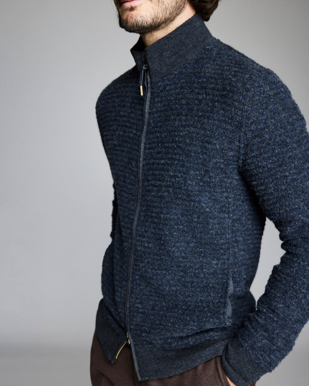 Man wearing a dark blue zip-up sweater against a gray background