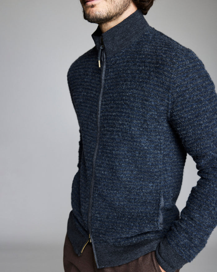 Man wearing a dark blue zip-up sweater against a gray background