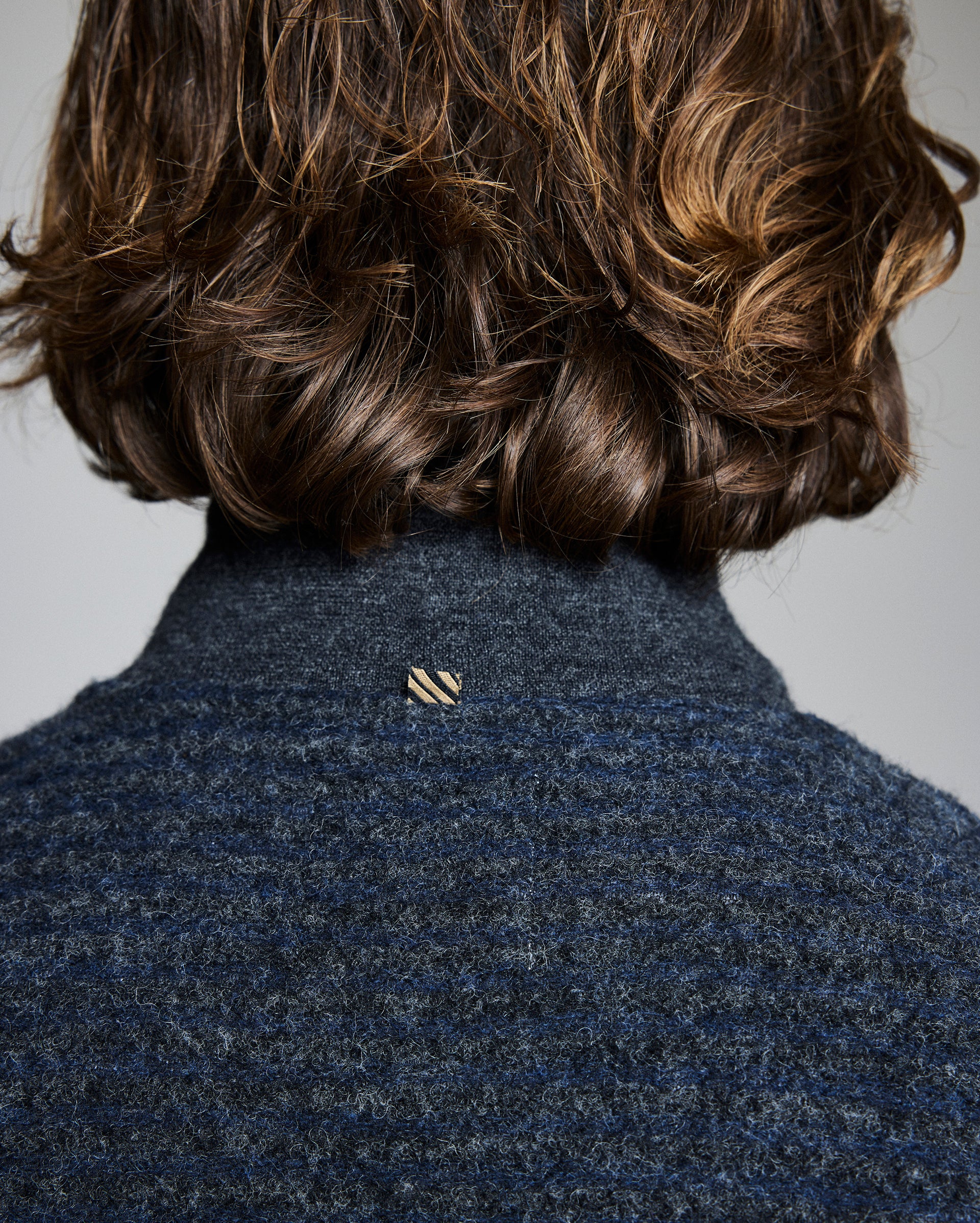 Person wearing a dark blue textured coat with a small logo on a plain background