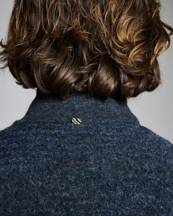 Person wearing a dark blue textured coat with a small logo on a plain background