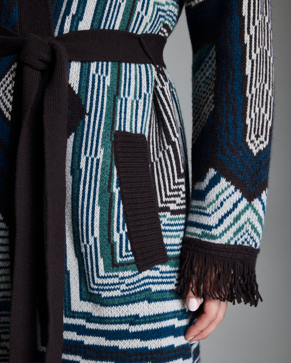 Close-up of a patterned coat with geometric design and fringed hem.