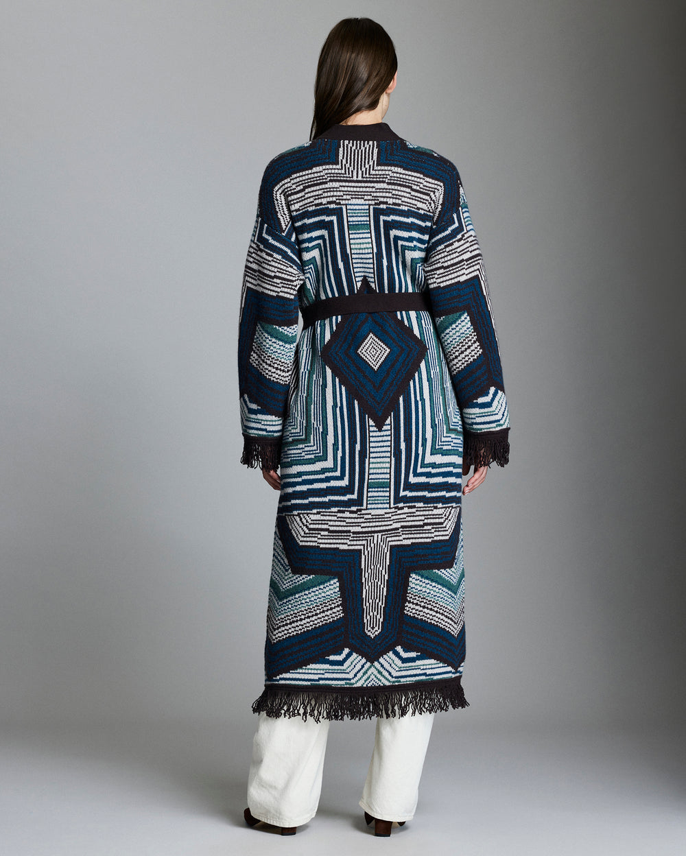 Person wearing a long, patterned coat with a geometric design on a gray background