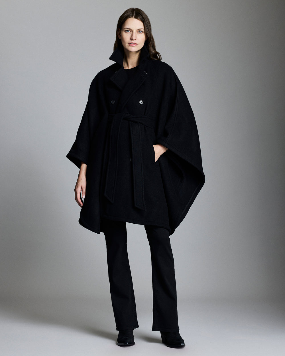 Woman wearing a black coat and pants against a gray background