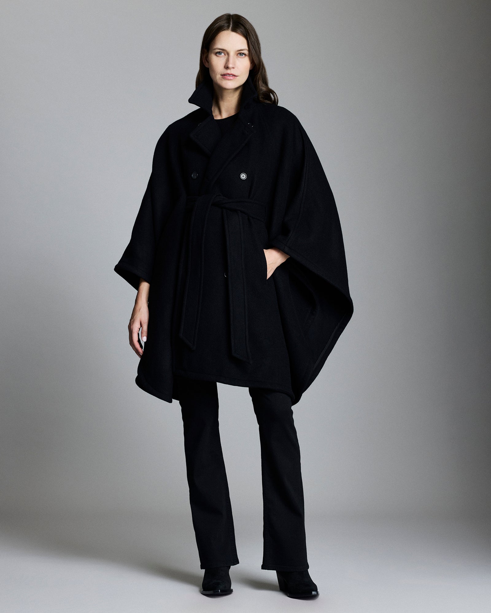 Woman wearing a black coat and pants against a gray background