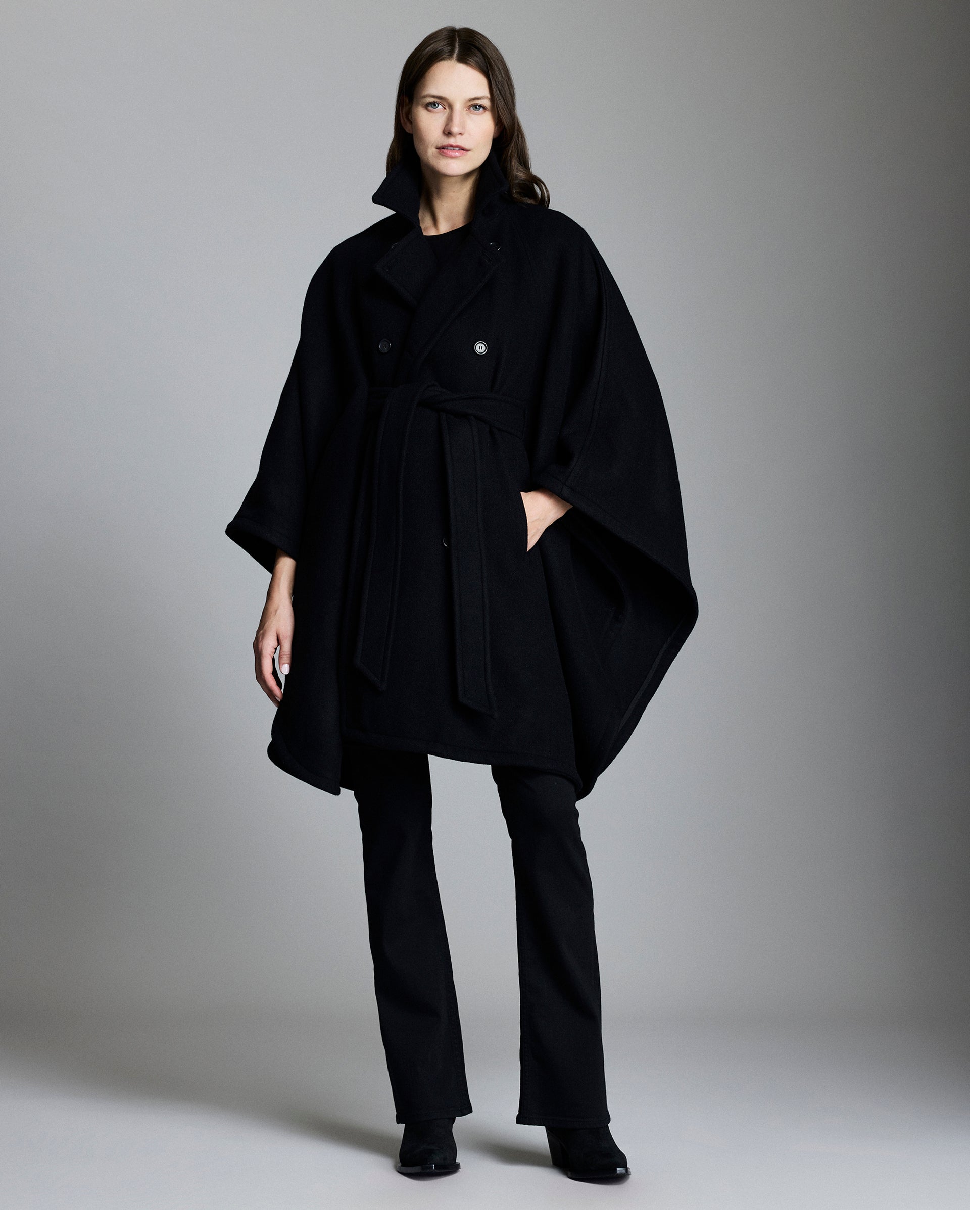 Woman wearing a black coat and pants against a gray background