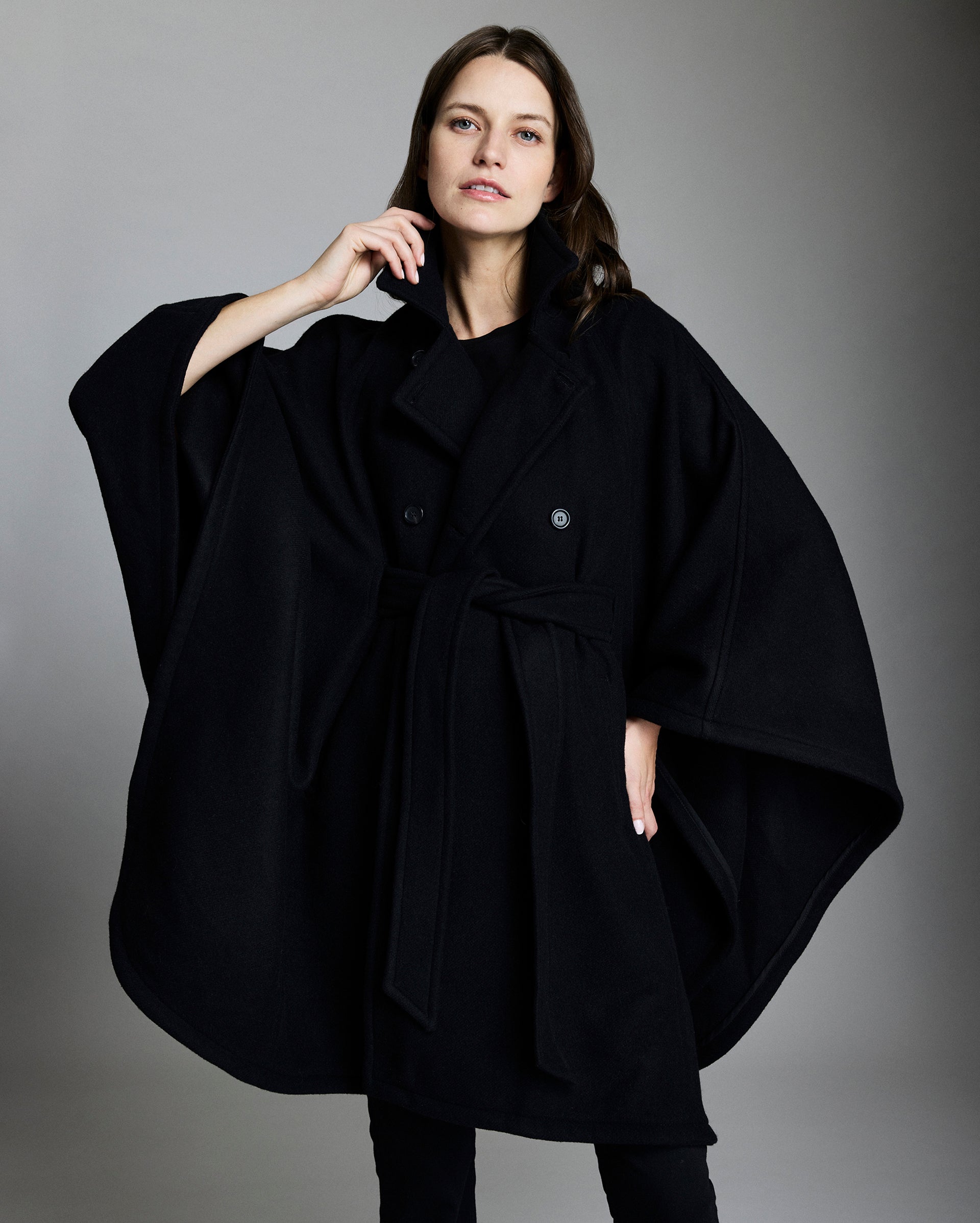 Woman wearing a black poncho against a gray background