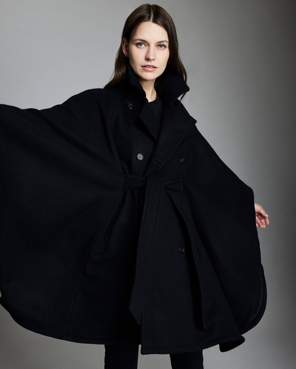Woman wearing a black cape against a gray background