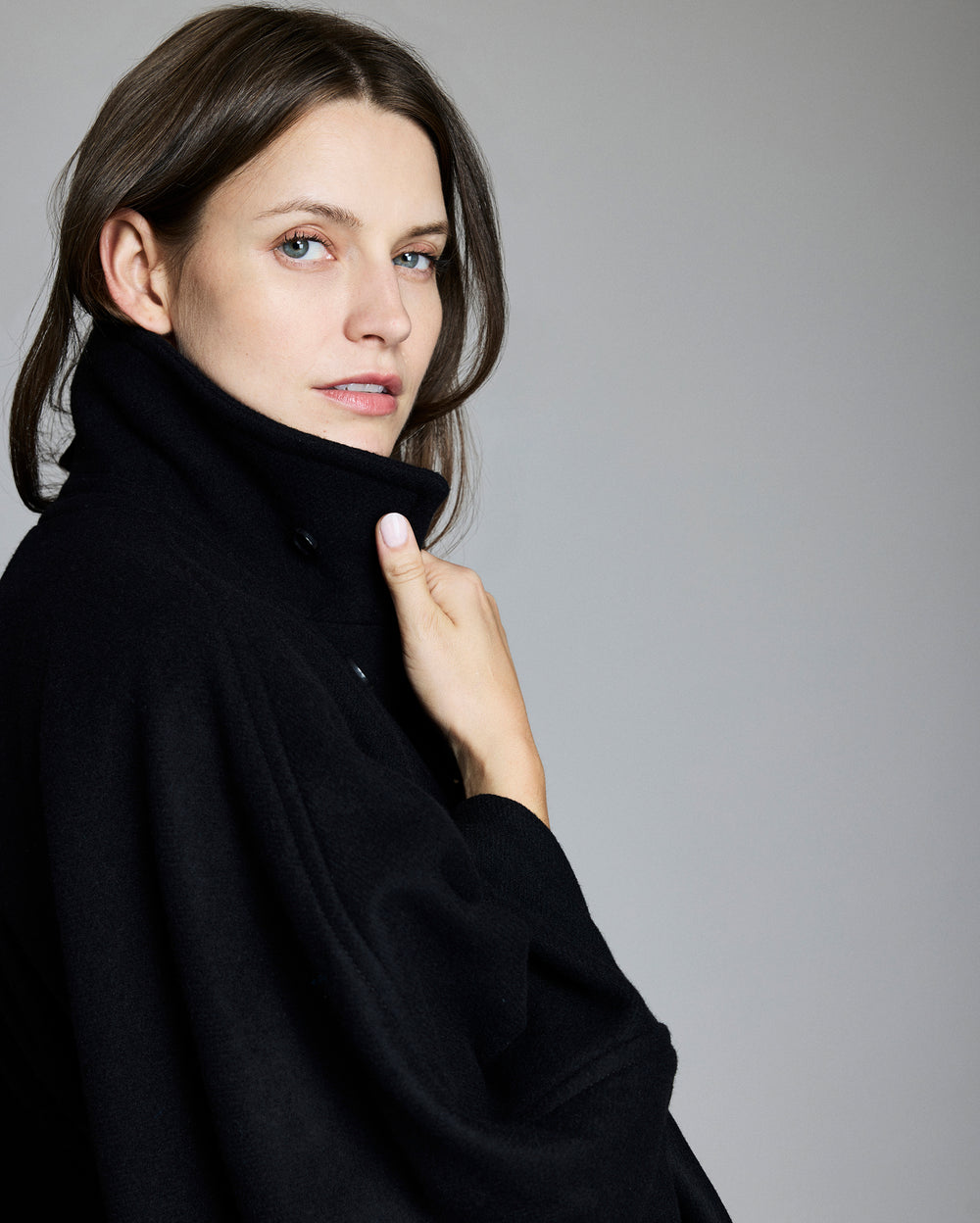 Woman wearing a black cape-style peacoat against a plain background