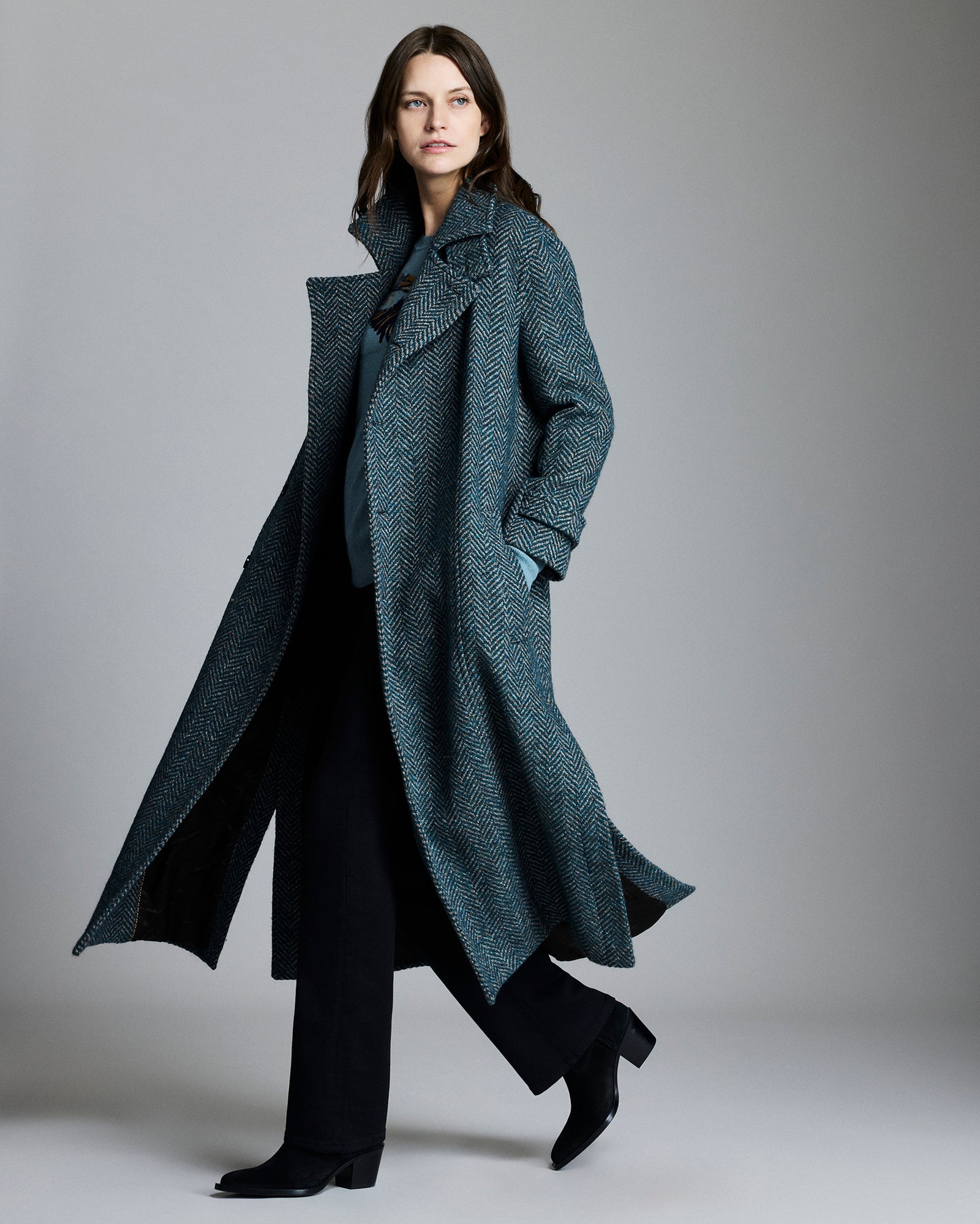 Woman wearing a long, dark gray coat against a plain background
