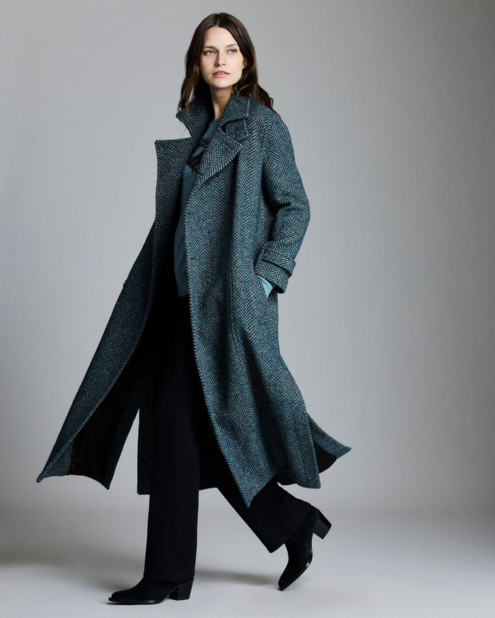 Woman wearing a long, dark gray coat against a plain background