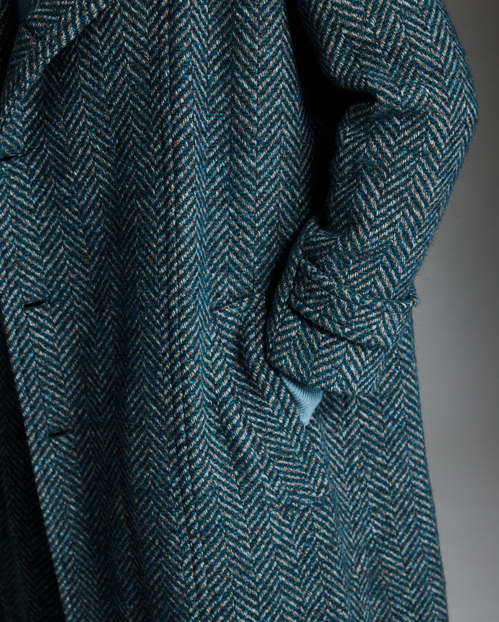 Close-up of a textured blue coat with a herringbone pattern on a dark background