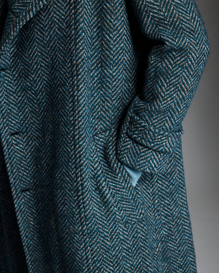 Close-up of a textured blue coat with a herringbone pattern on a dark background