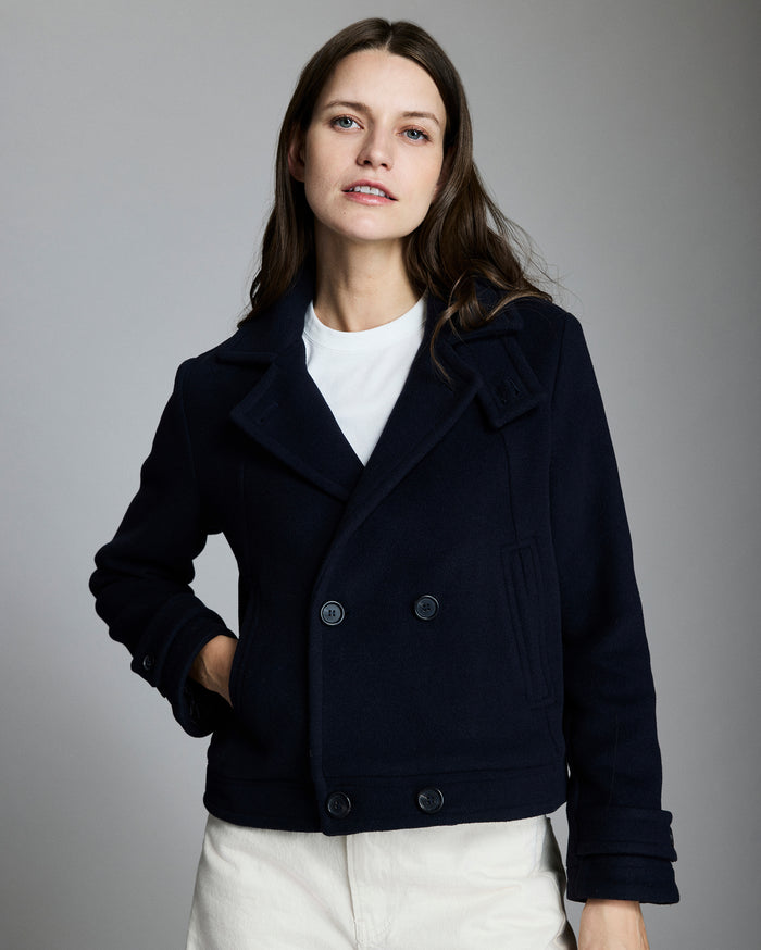 Woman wearing a dark blue peacoat over a white shirt on a gray background