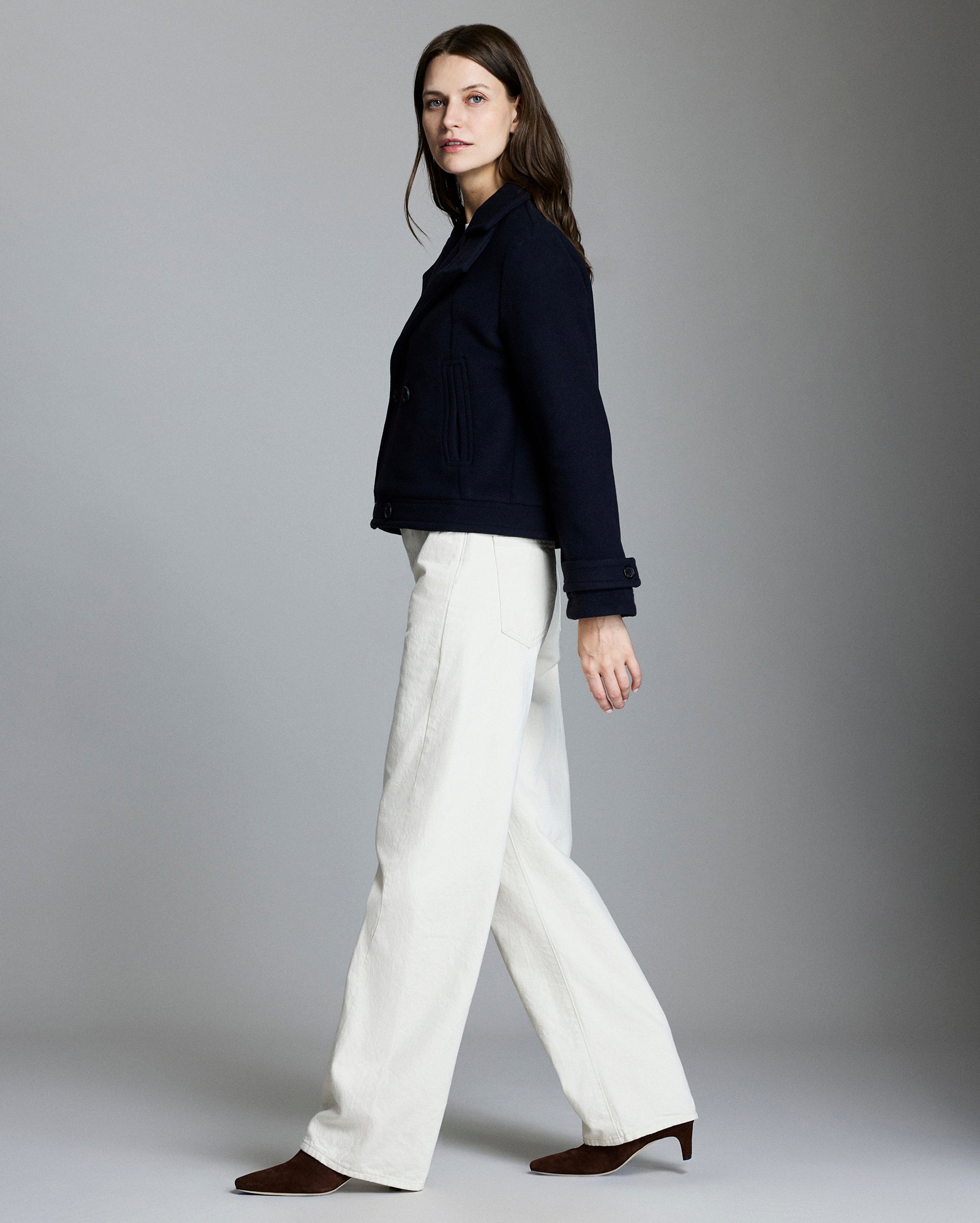 Woman wearing a navy jacket and white pants on a gray background