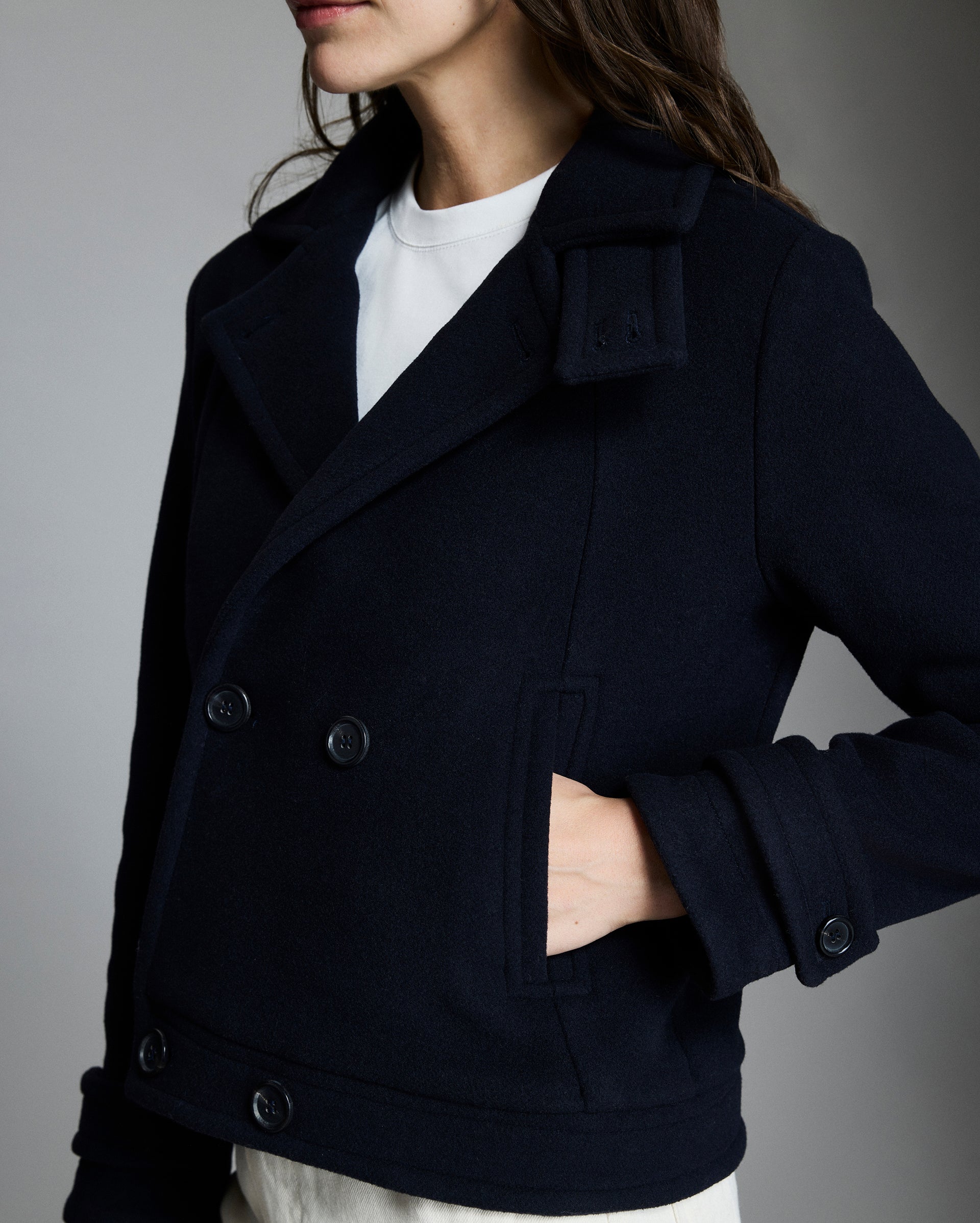 Navy peacoat worn by a person on a gray background