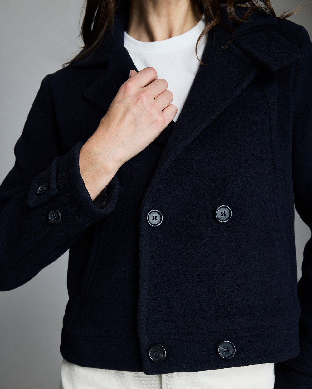 Person wearing a black peacoat with a plain background