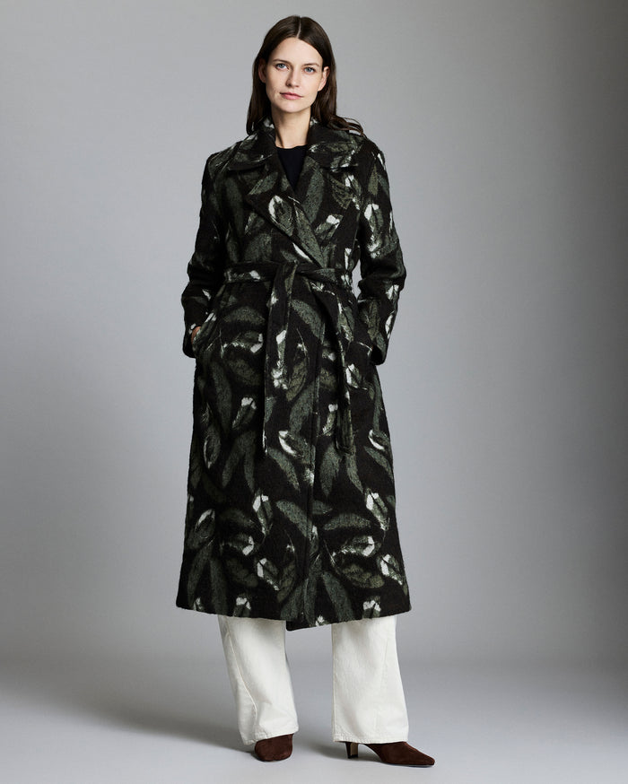 Woman wearing a black patterned coat with white pants on a gray background