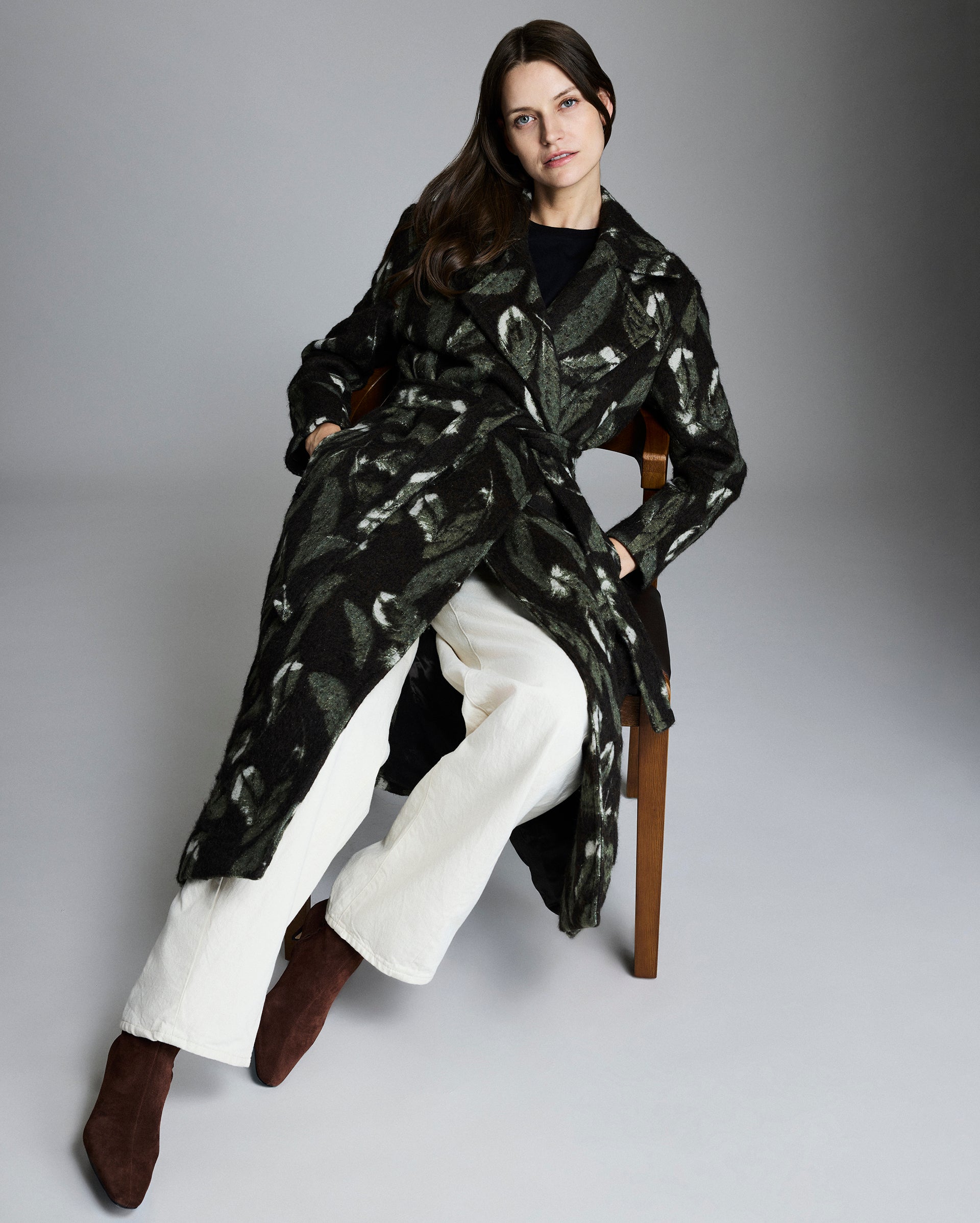 Woman wearing a black and white patterned coat sitting on a chair against a gray background
