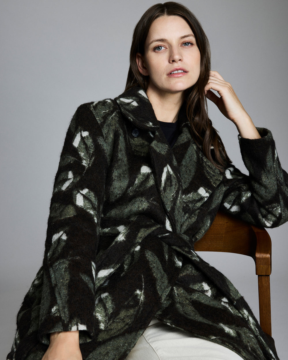 Woman wearing a black and white patterned coat sitting on a chair against a gray background