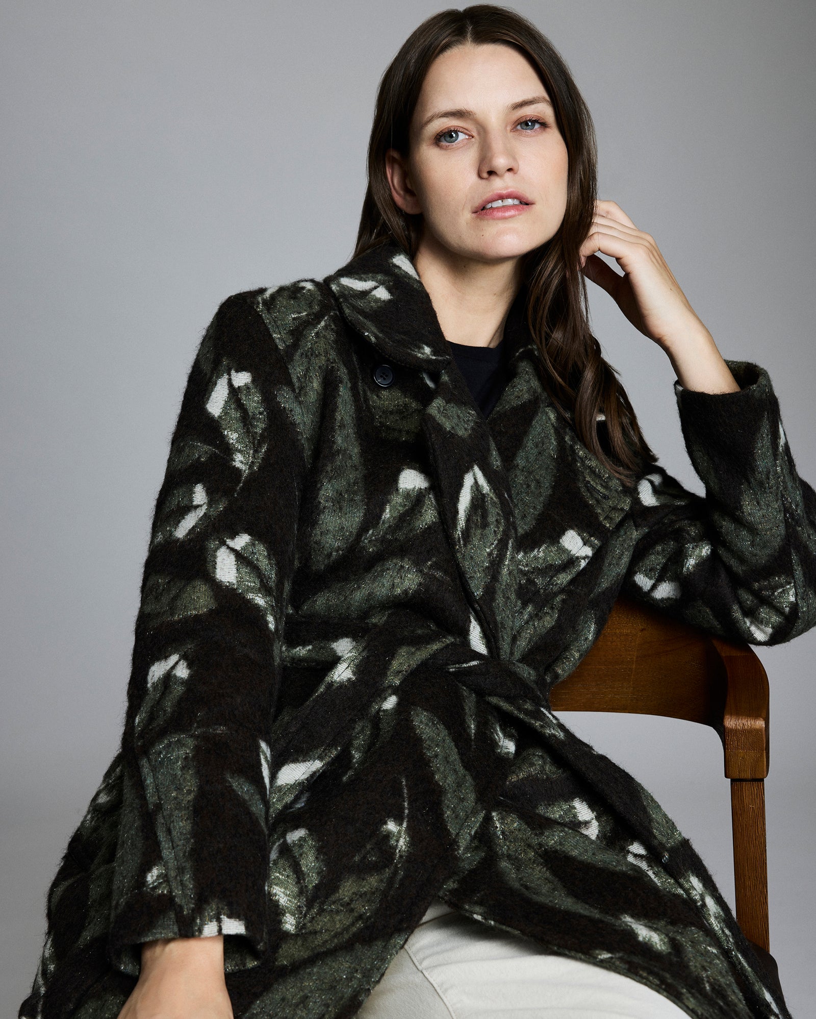 Woman wearing a black and white patterned coat sitting on a chair against a gray background