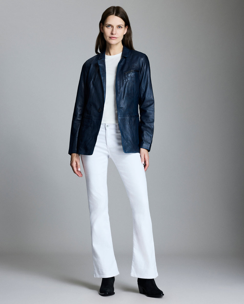 Woman wearing a navy jacket, white shirt, and white pants on a gray background