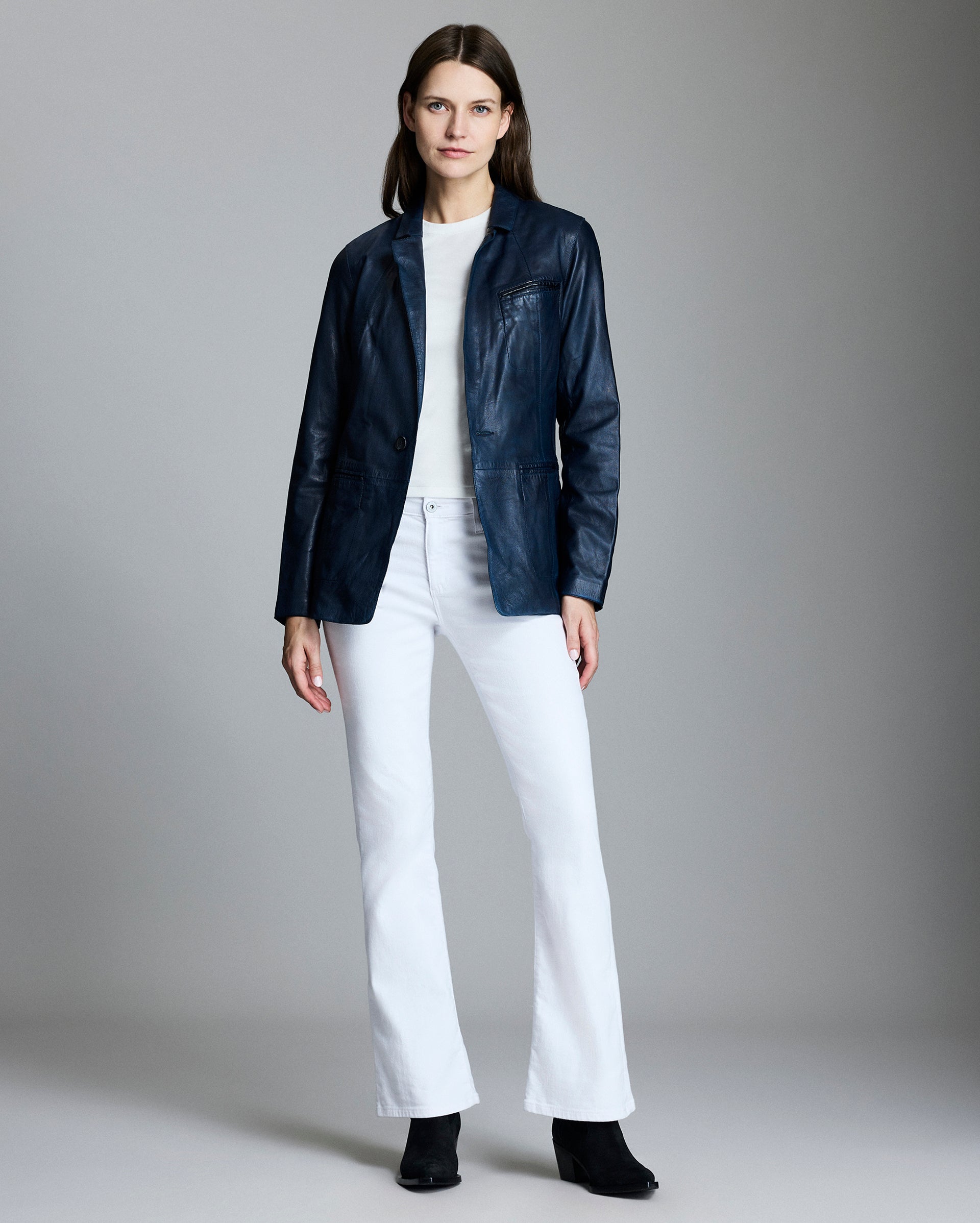 Woman wearing a navy jacket, white shirt, and white pants on a gray background