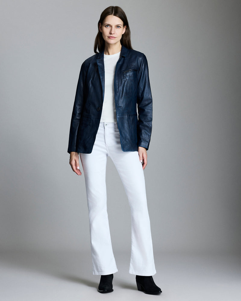 Woman wearing a navy jacket, white shirt, and white pants on a gray background Alternate