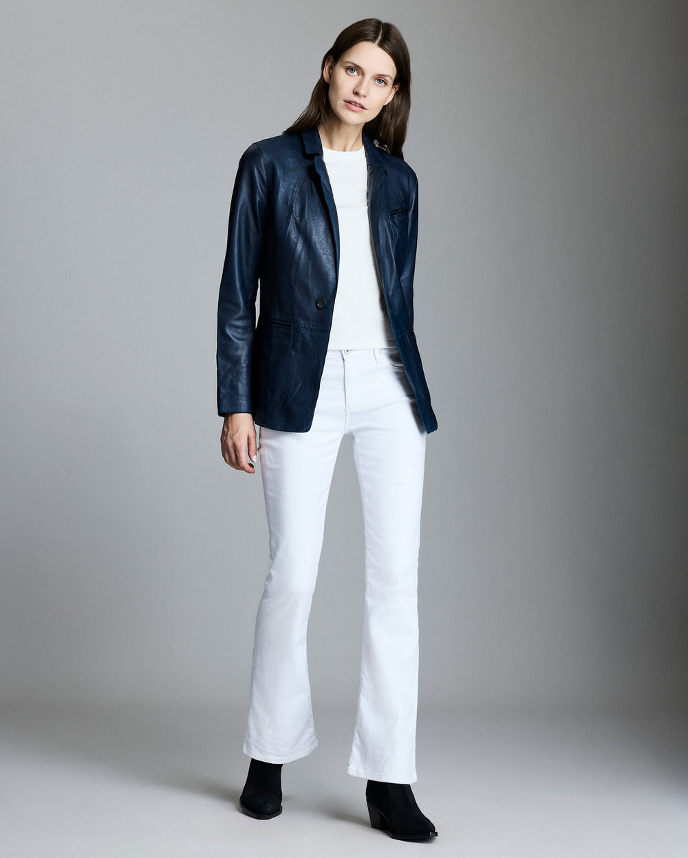 Woman wearing a navy jacket, white shirt, and white pants on a gray background