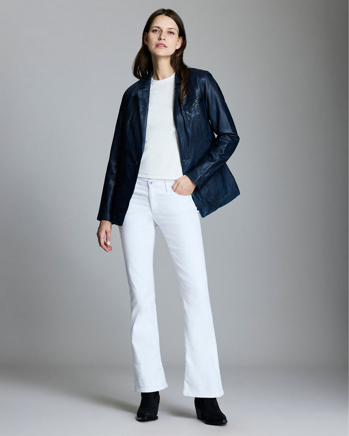 Woman wearing a navy jacket, white shirt, and white pants on a gray background