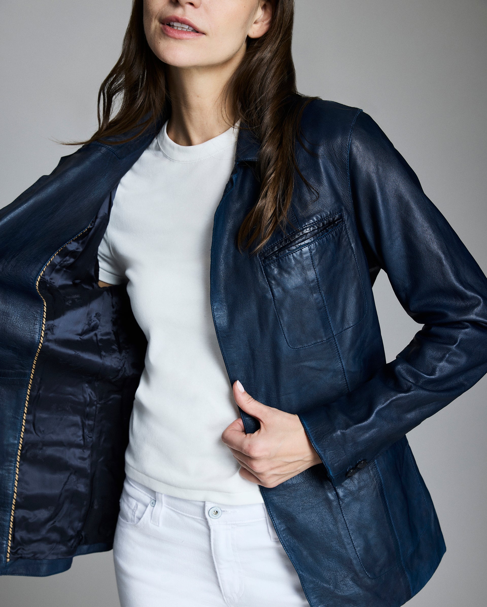 Woman wearing a navy blue jacket over a white shirt and pants on a gray background