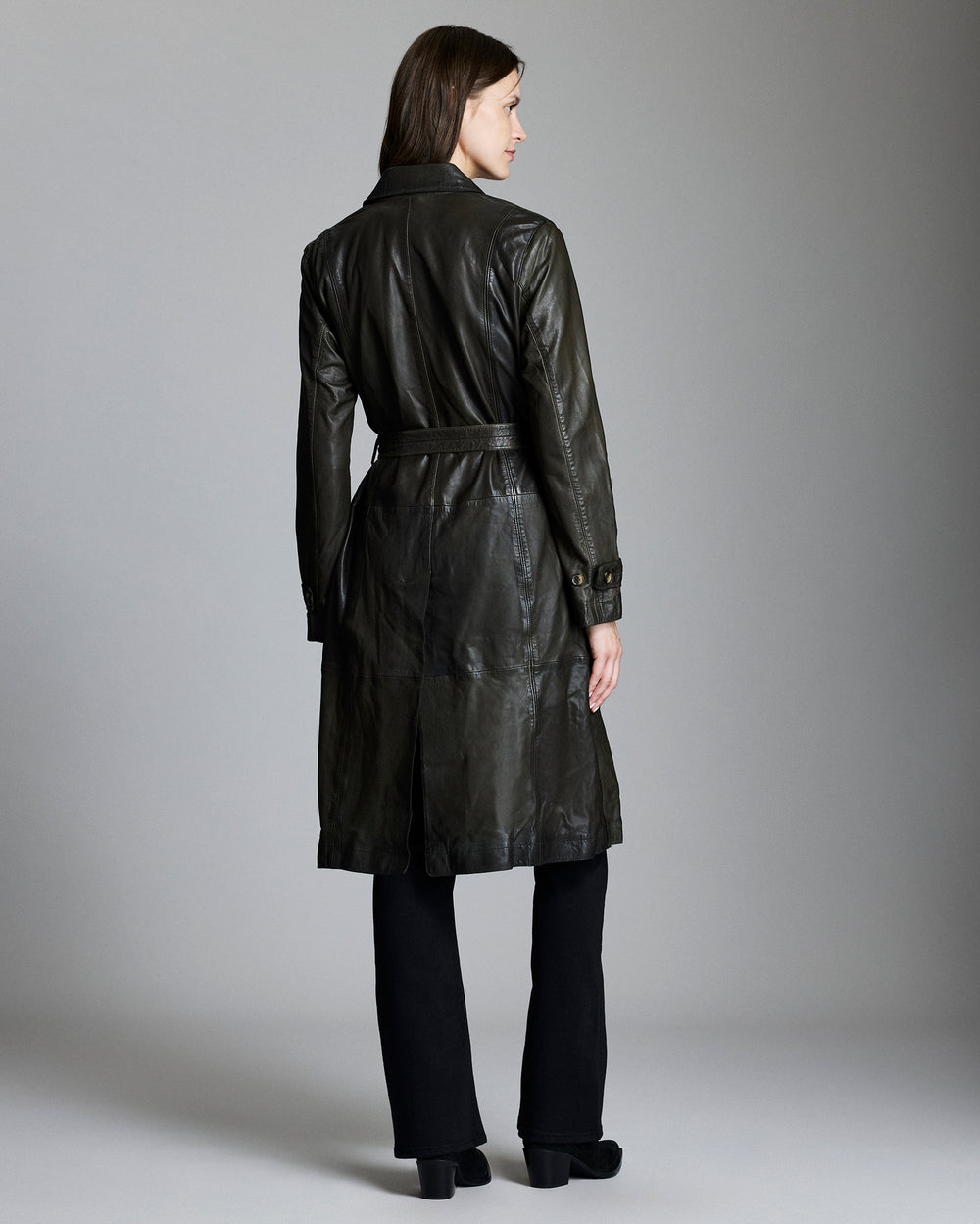 Woman wearing a black leather trench coat against a gray background