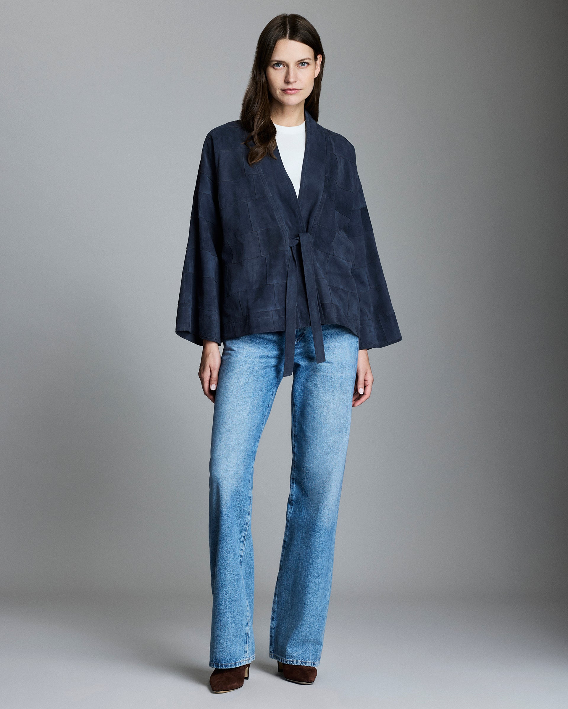 Woman wearing a navy jacket and blue jeans against a gray background