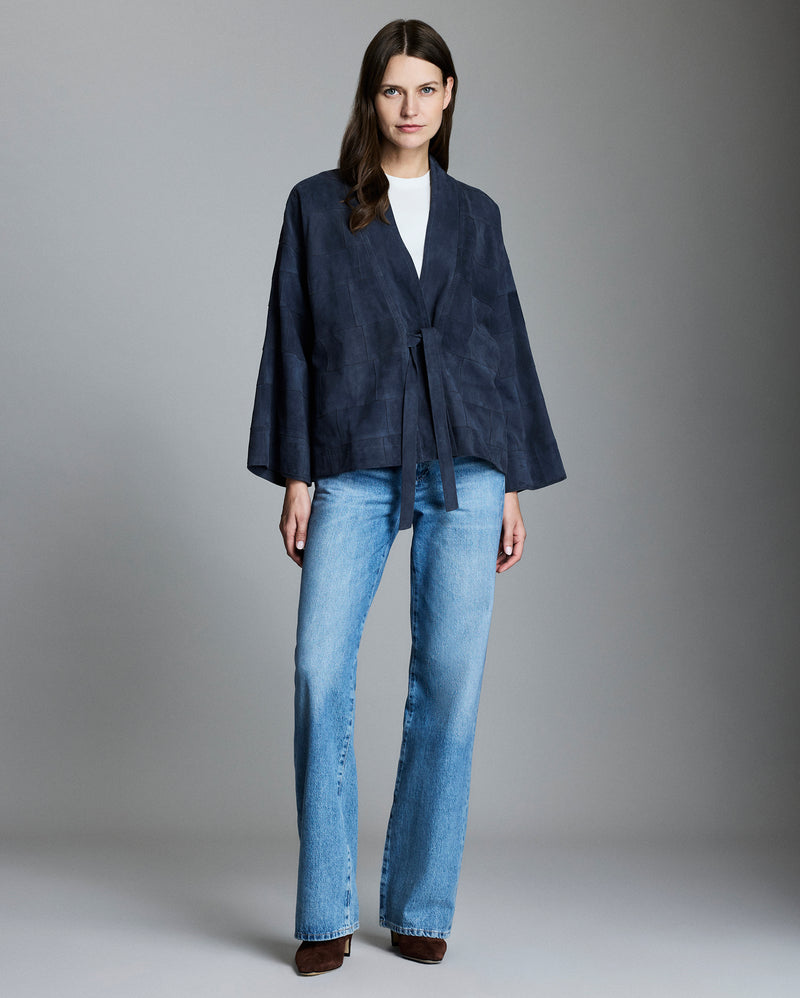 Woman wearing a navy jacket and blue jeans against a gray background Alternate