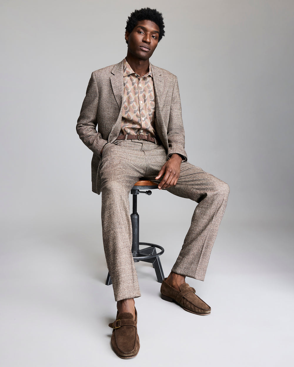 Model wears the wool silk walton jacket as he sits on a stool.