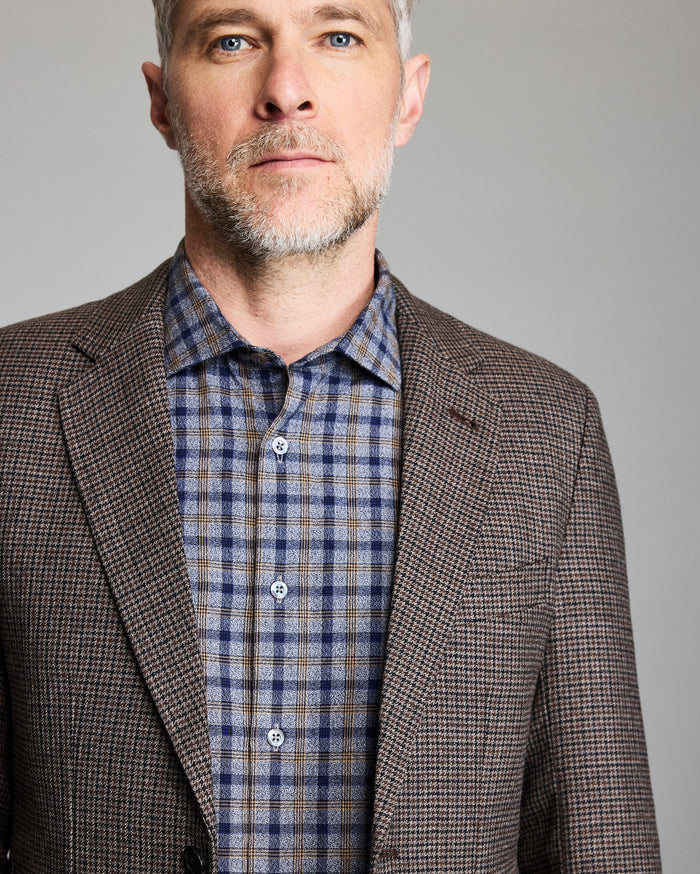 Man wearing a brown checkered blazer over a plaid shirt against a gray background