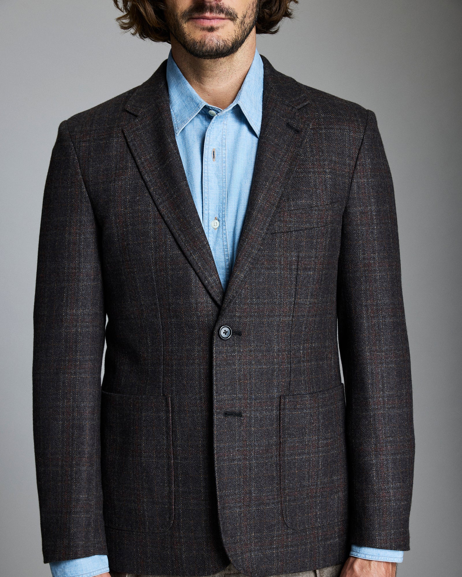 Man wearing a brown checkered blazer over a light blue shirt on a gray background